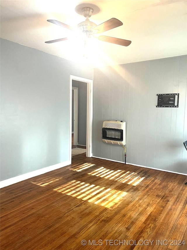 spare room featuring heating unit, ceiling fan, wooden walls, and dark hardwood / wood-style floors