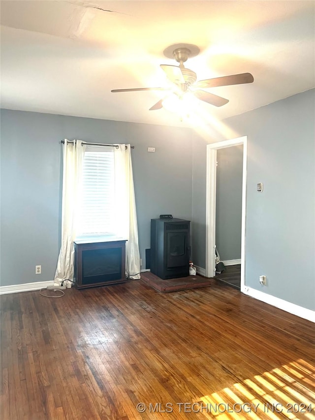 unfurnished room with dark hardwood / wood-style floors, ceiling fan, and a wood stove