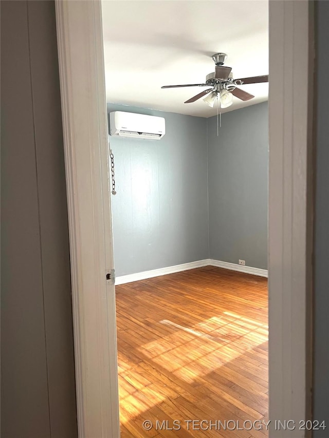 unfurnished room with hardwood / wood-style flooring, a wall unit AC, and ceiling fan