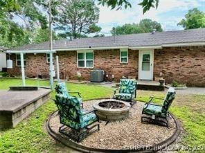 back of property with a lawn, a fire pit, and central AC