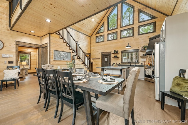 dining area with a wealth of natural light, high vaulted ceiling, wood walls, and light wood-type flooring