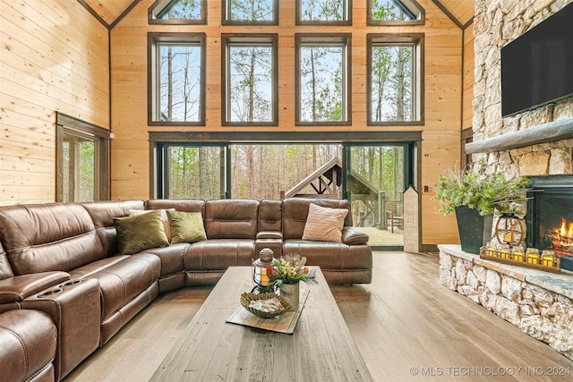 living room with wood walls, a stone fireplace, light wood-type flooring, and high vaulted ceiling