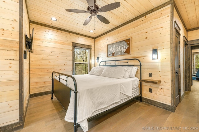 bedroom featuring hardwood / wood-style flooring, ceiling fan, wood walls, and multiple windows