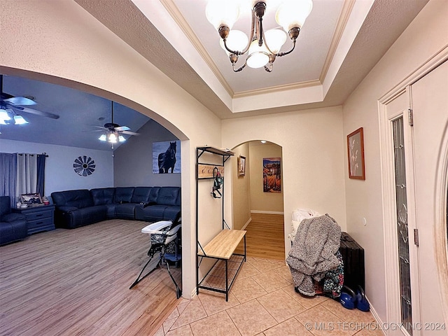 living room with ceiling fan with notable chandelier, light wood-type flooring, ornamental molding, and a tray ceiling