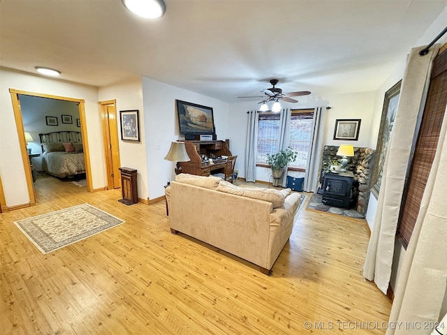 living room featuring ceiling fan, a wood stove, and light hardwood / wood-style flooring