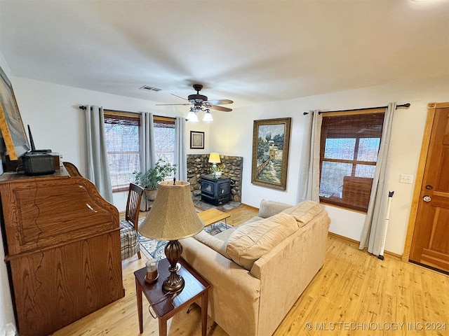 living room featuring light hardwood / wood-style floors, a wood stove, and ceiling fan