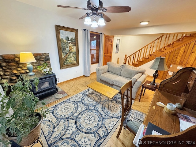 living room featuring ceiling fan, a wood stove, and light hardwood / wood-style flooring