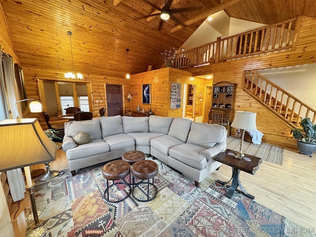 living room featuring hardwood / wood-style flooring, ceiling fan with notable chandelier, wood walls, and high vaulted ceiling