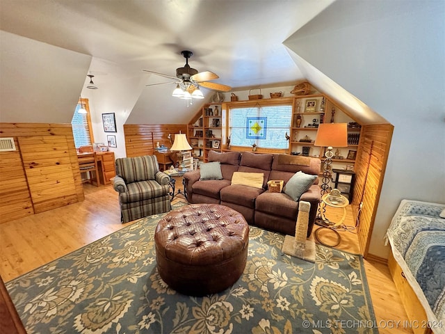 living room with wood walls, ceiling fan, vaulted ceiling, and light wood-type flooring