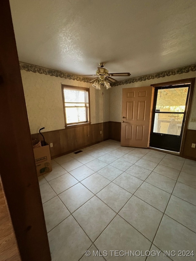 tiled empty room featuring a textured ceiling, wooden walls, and ceiling fan