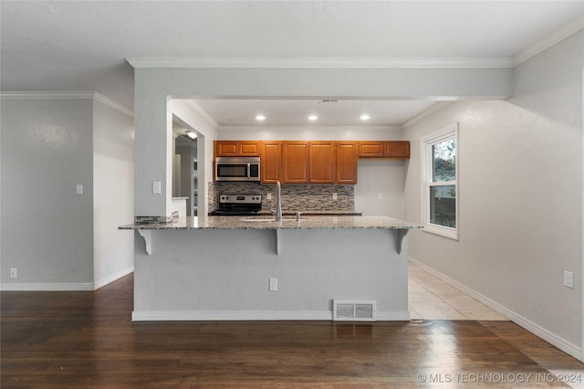 kitchen with a breakfast bar area, hardwood / wood-style flooring, light stone countertops, and appliances with stainless steel finishes