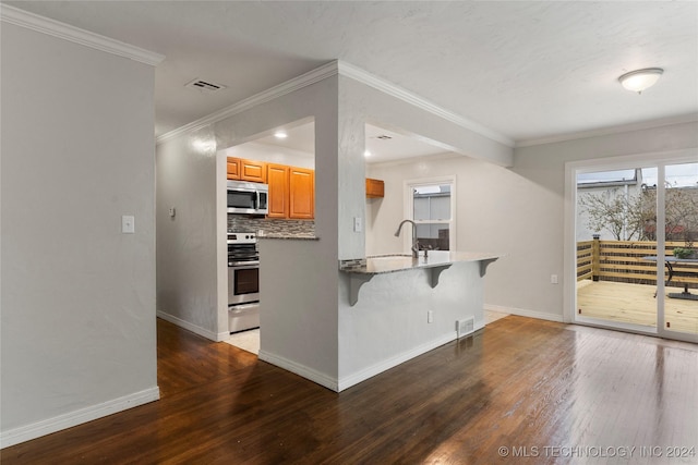 kitchen featuring dark hardwood / wood-style floors, decorative backsplash, ornamental molding, appliances with stainless steel finishes, and a breakfast bar area