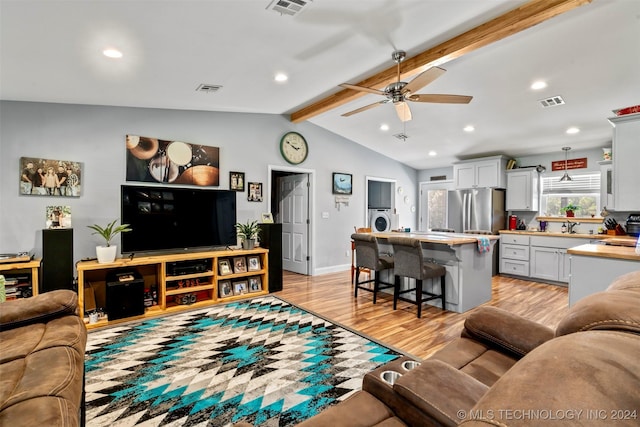 living room featuring washer / dryer, sink, lofted ceiling with beams, light wood-type flooring, and ceiling fan