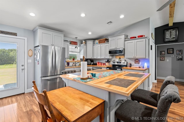 kitchen with butcher block countertops, a breakfast bar, appliances with stainless steel finishes, light hardwood / wood-style floors, and vaulted ceiling