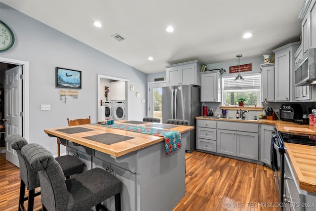 kitchen featuring stainless steel appliances, butcher block counters, washing machine and clothes dryer, and gray cabinets