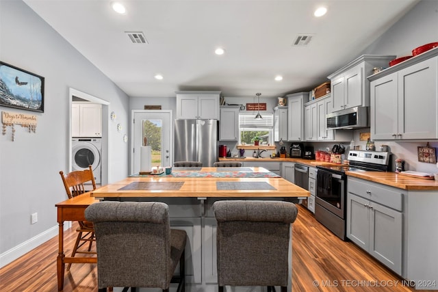 kitchen featuring butcher block counters, washer / dryer, gray cabinets, stainless steel appliances, and hardwood / wood-style floors