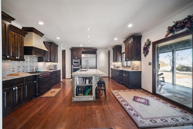 kitchen featuring dark hardwood / wood-style flooring, tasteful backsplash, custom range hood, stainless steel appliances, and a center island with sink