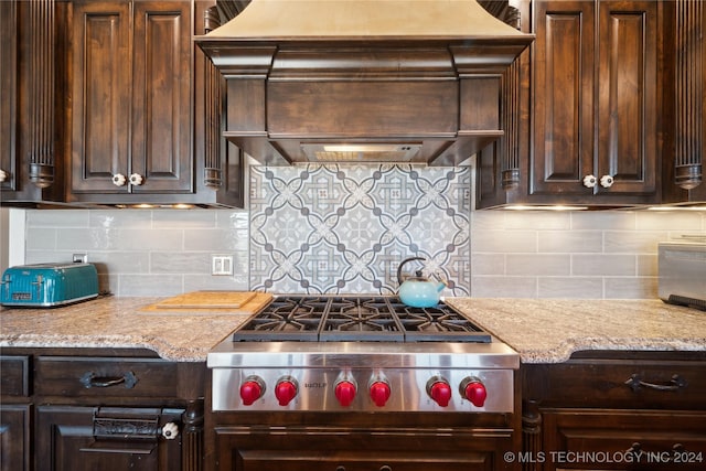 kitchen featuring light stone countertops, backsplash, premium range hood, dark brown cabinetry, and stainless steel gas cooktop