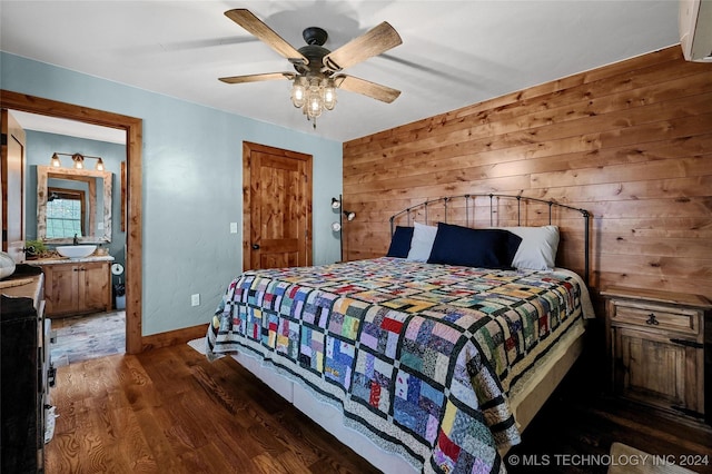 bedroom with dark hardwood / wood-style floors, ceiling fan, wooden walls, and ensuite bath