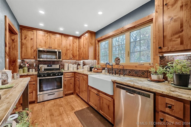 kitchen featuring sink, light stone counters, light hardwood / wood-style flooring, decorative backsplash, and appliances with stainless steel finishes