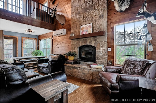 living room featuring high vaulted ceiling, a wall unit AC, wood walls, hardwood / wood-style floors, and a fireplace