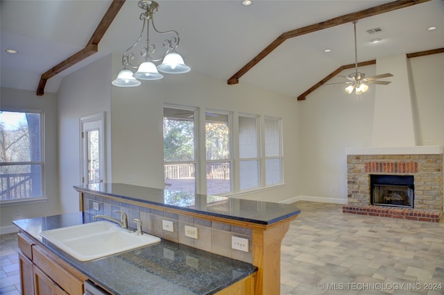 kitchen with a brick fireplace, sink, pendant lighting, vaulted ceiling with beams, and an island with sink