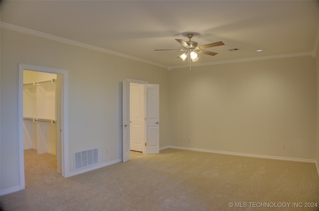 unfurnished bedroom with a spacious closet, ceiling fan, light colored carpet, a closet, and ornamental molding