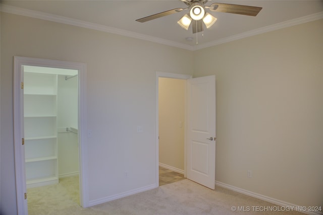 unfurnished bedroom with a spacious closet, ceiling fan, crown molding, light carpet, and a closet