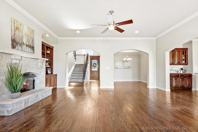 unfurnished living room featuring a stone fireplace, built in features, dark hardwood / wood-style floors, ceiling fan with notable chandelier, and ornamental molding