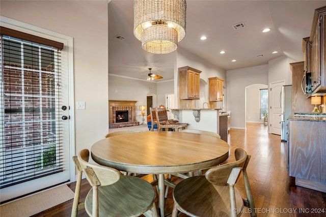 dining room with crown molding, a fireplace, dark wood-type flooring, and ceiling fan with notable chandelier