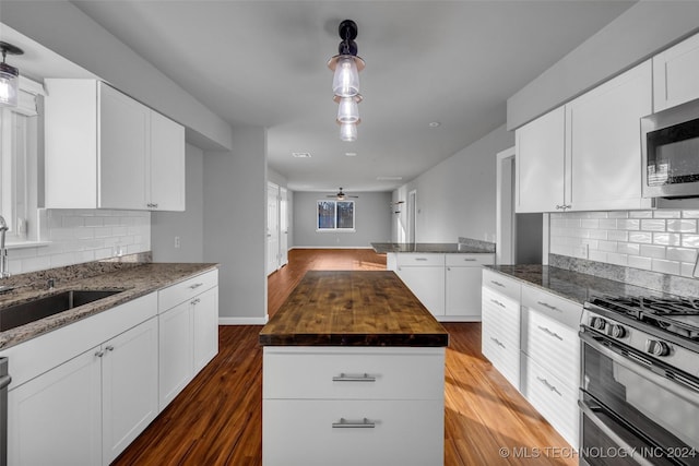 kitchen with appliances with stainless steel finishes, sink, wood-type flooring, white cabinets, and a kitchen island