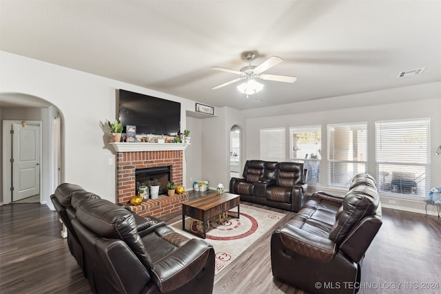 living room with dark hardwood / wood-style flooring, a brick fireplace, and ceiling fan