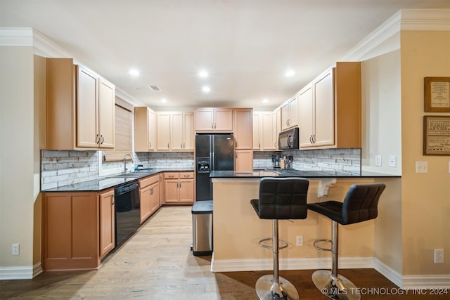 kitchen with kitchen peninsula, crown molding, a breakfast bar, black appliances, and light wood-type flooring