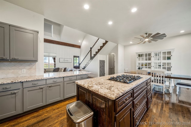 kitchen featuring stainless steel gas stovetop, backsplash, dark hardwood / wood-style floors, ceiling fan, and light stone counters