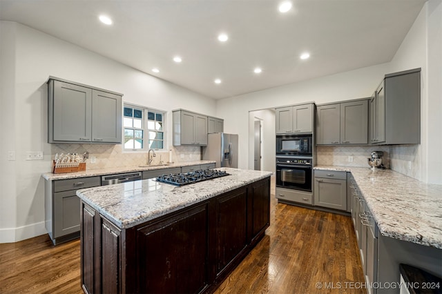 kitchen with light stone countertops, dark wood-type flooring, sink, black appliances, and a center island