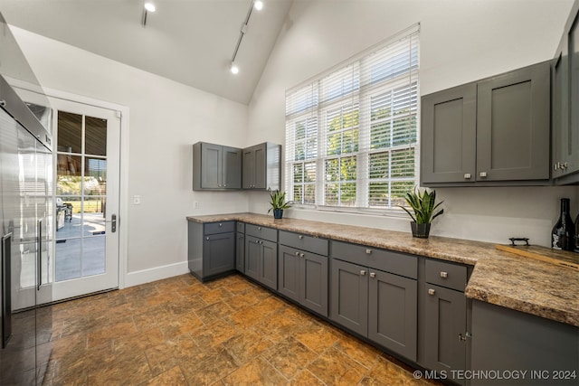 kitchen featuring gray cabinetry, stone counters, rail lighting, and lofted ceiling