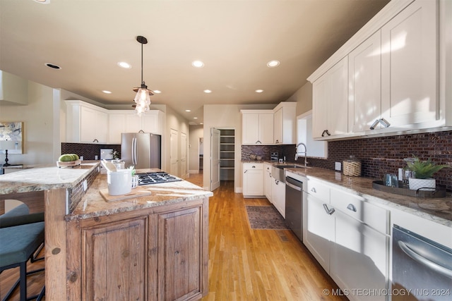 kitchen with white cabinetry, stainless steel appliances, light stone counters, pendant lighting, and a kitchen island