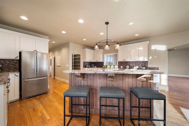 kitchen with stainless steel fridge, light stone countertops, white cabinetry, and light hardwood / wood-style flooring