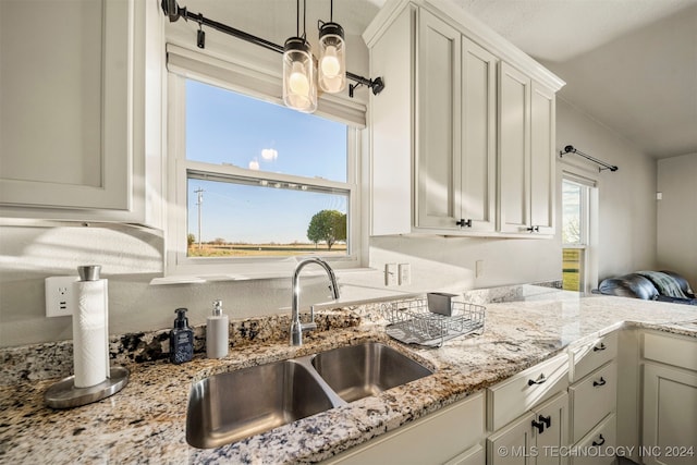 kitchen with light stone countertops, white cabinetry, and sink