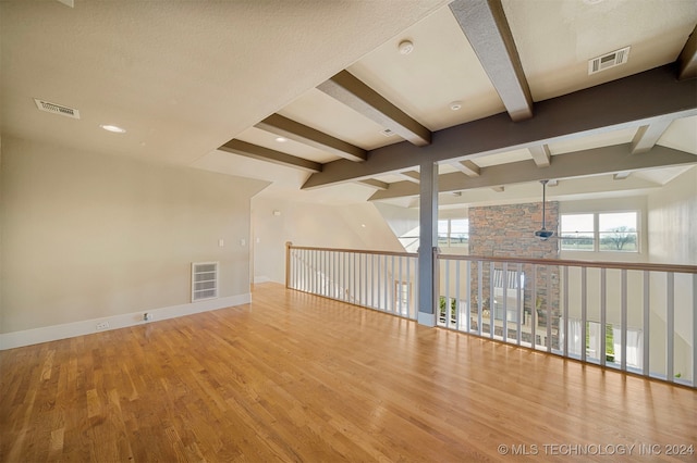 unfurnished room with beam ceiling, a textured ceiling, and light wood-type flooring