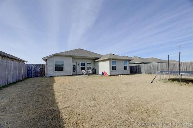 rear view of property with a lawn, a patio area, and a trampoline