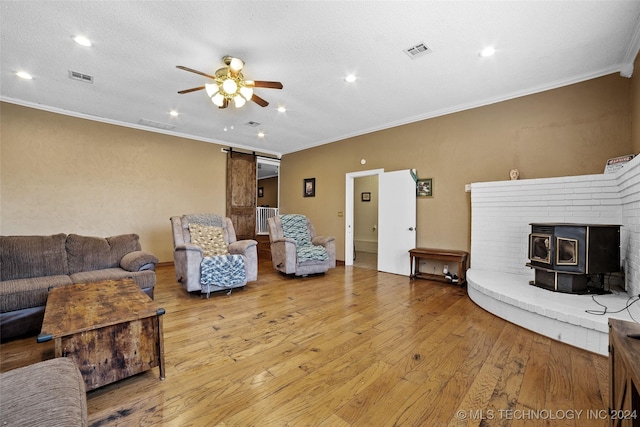 living room featuring a textured ceiling, light wood-type flooring, ornamental molding, ceiling fan, and a barn door