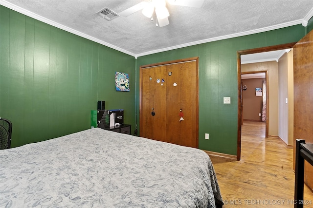 bedroom with wood walls, ceiling fan, crown molding, a textured ceiling, and a closet