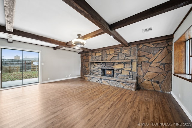 unfurnished living room with beamed ceiling, a stone fireplace, and hardwood / wood-style floors