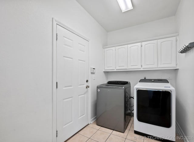 clothes washing area with washer and clothes dryer, cabinets, and light tile patterned floors