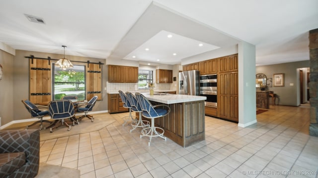 kitchen featuring a center island, hanging light fixtures, tasteful backsplash, a barn door, and appliances with stainless steel finishes