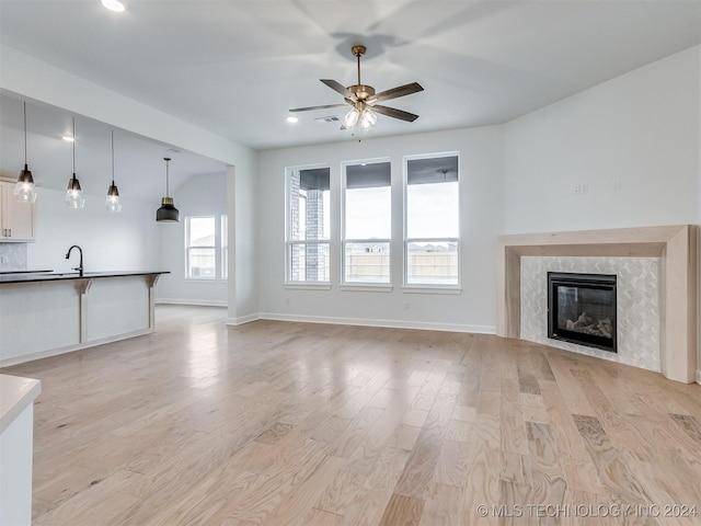 unfurnished living room with a high end fireplace, light hardwood / wood-style flooring, and ceiling fan