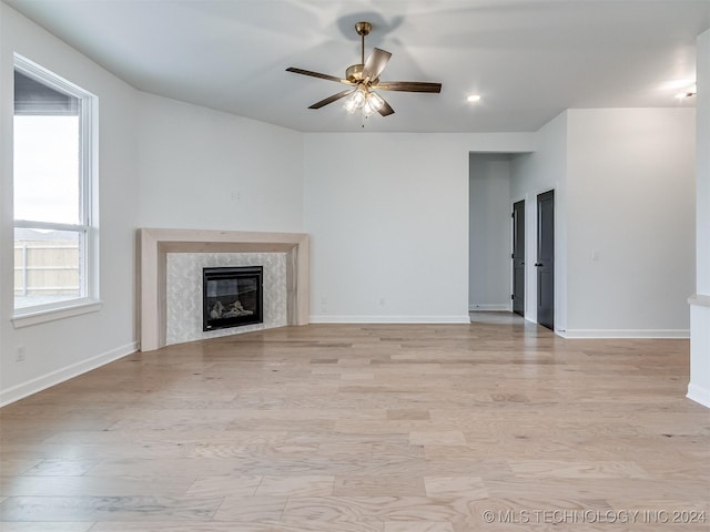 unfurnished living room with ceiling fan, a high end fireplace, and light hardwood / wood-style floors