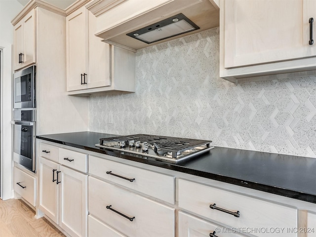 kitchen with tasteful backsplash, light wood-type flooring, cream cabinetry, appliances with stainless steel finishes, and custom exhaust hood