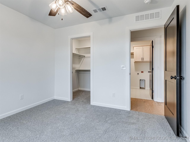 unfurnished bedroom featuring light carpet, a walk in closet, a closet, and ceiling fan